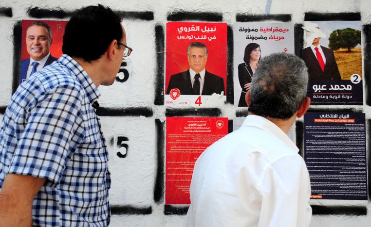 Men watch a campaign poster of the owner of the Tunisian private channel Nessma TV, Nabil Karoui (C)