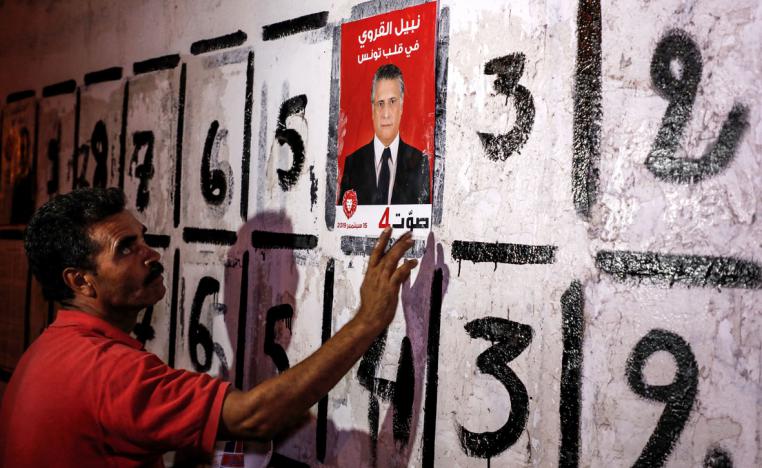 A supporter of the Tunisian businessperson and media mogul Nabil Karoui sticks a campaign poster to a wall