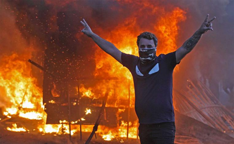 A protester flashes the V for victory sign as a riot police vehicle burns behind him during protests in Baghdad