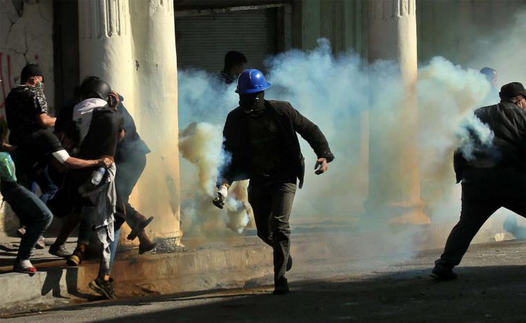 An anti-government protester runs with a tear gas canister fired by police during clashes in Baghdad