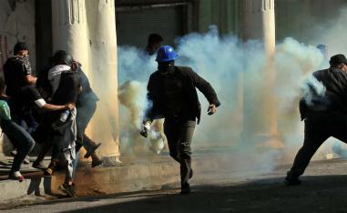 An anti-government protester runs with a tear gas canister fired by police during clashes in Baghdad