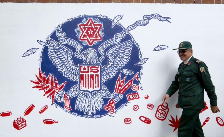 A member of Iran's Revolutionary Guards walks past a new mural painted on the walls of the formar US embassy in the capital Tehran