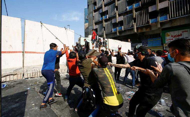 Iraqi demonstrators try to push down a concrete wall during ongoing anti-government protests in Baghdad