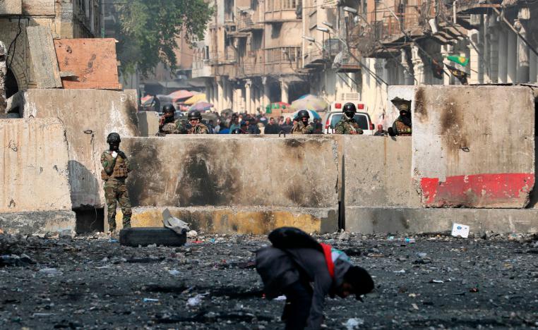 An anti-government protester picks up stones as security forces close Rasheed Street during protests in Baghdad