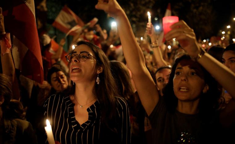 Women gesture and carry candles as they march during ongoing anti-government protests in Beirut