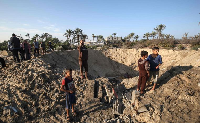 Palestinian children stand around a crater caused by an Israeli airstrike
