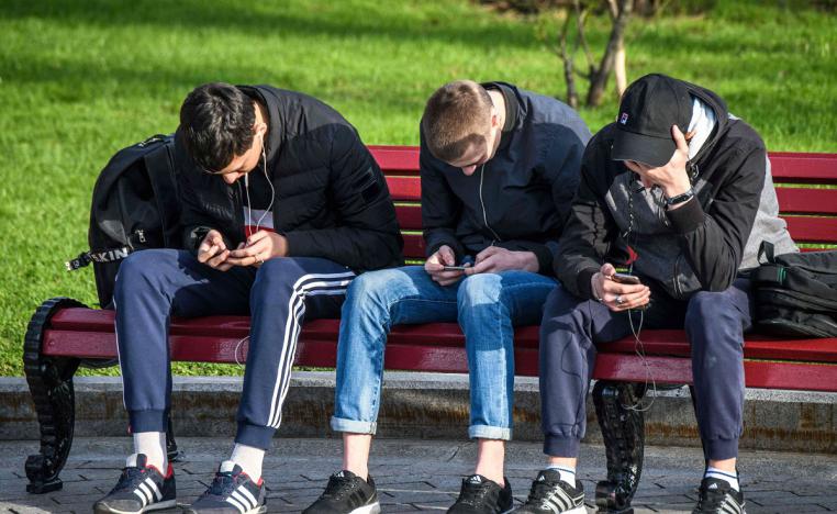 مراهقون روس يستعملون هواتفهم في جلسة بحديقة عامة