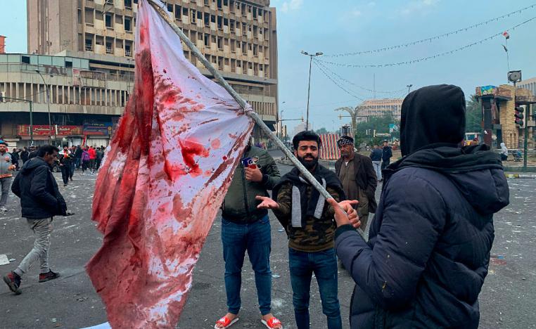 A protester holds a blood-stained flag at the site of an attack by gunmen in Baghdad