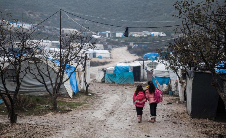 Children walk along a mudpath at a camp for displaced Syrians