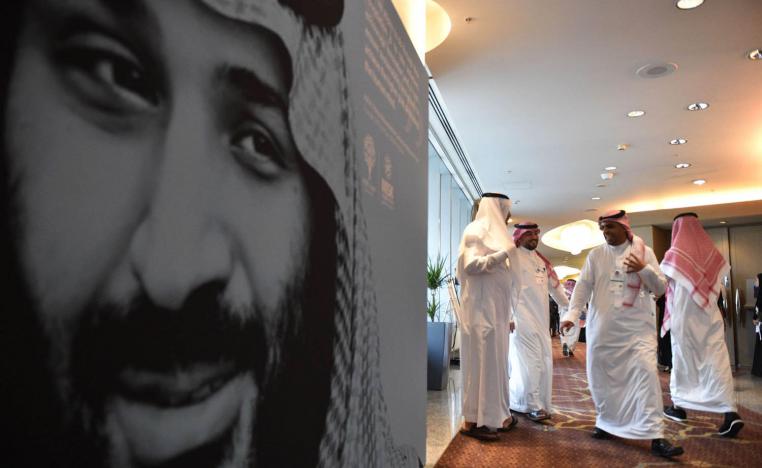 سعوديون يمرون بجانب صورة كبيرة لولي العهد الأمير محمد بن سلمان