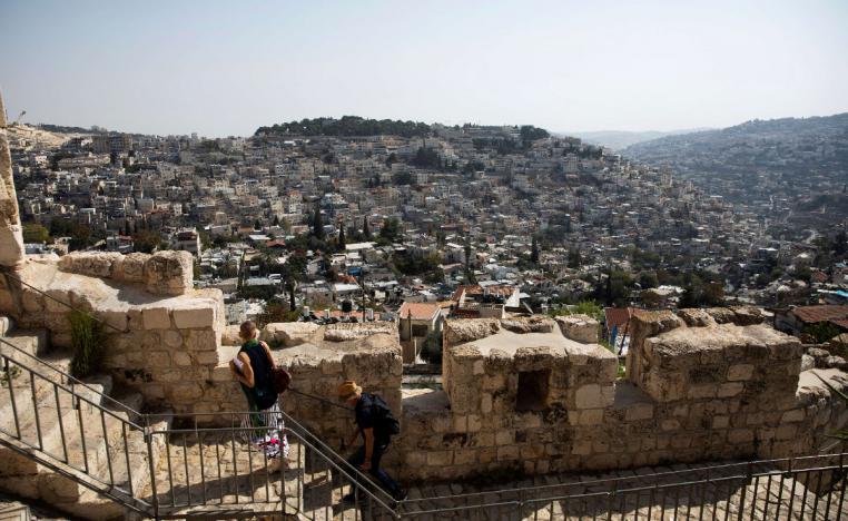 The Palestinian neighborhood of Silwan is seen in the background as people walk on a promenade on the surrounding walls of Jerusalem's Old City