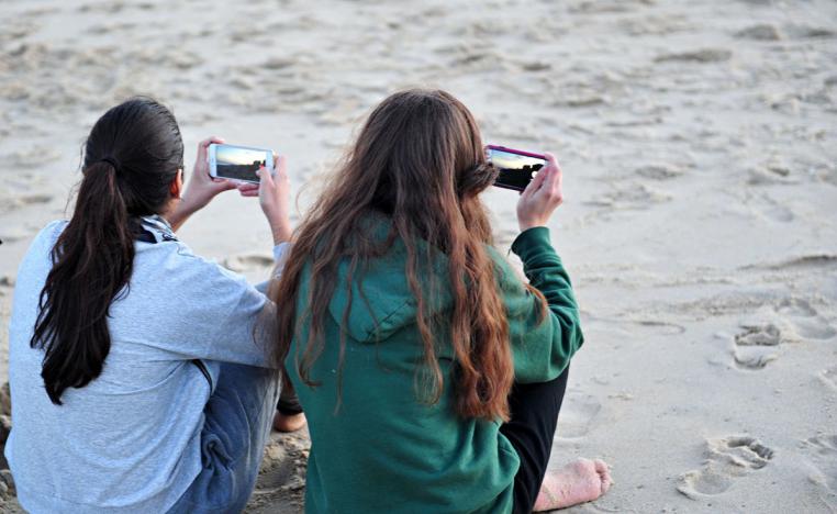 فتاتان تستخدمان هاتفيهما على أحد الشواطئ