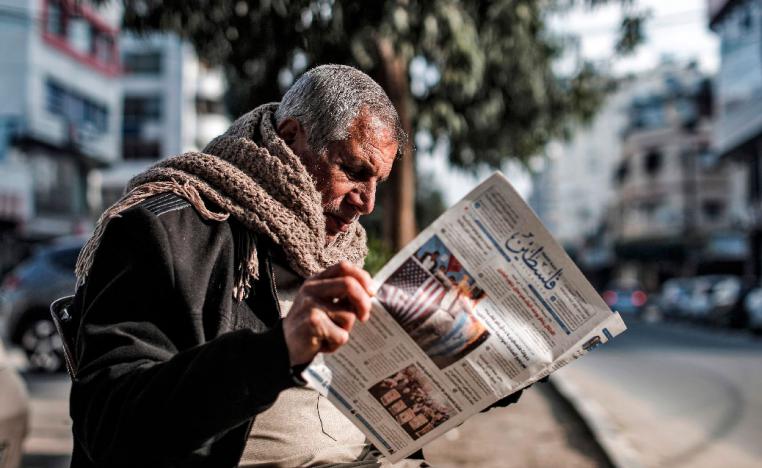 A Palestinian reads the "Filastin" (Palestine) daily newspaper while sitting along a street in Gaza City