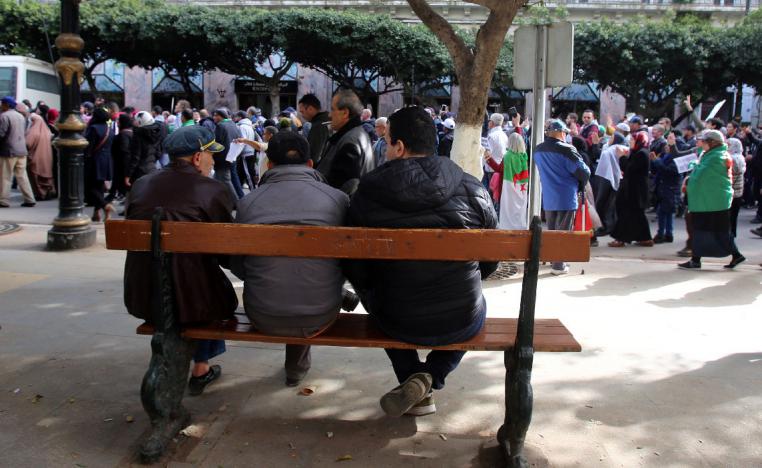People sit on a bench as protesters demanding a change of the power structure march in Algiers
