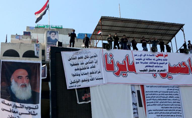 Iraqi anti-government protesters gather on a rooftop with posters bearing images of Grand Ayatollah Ali Sistani