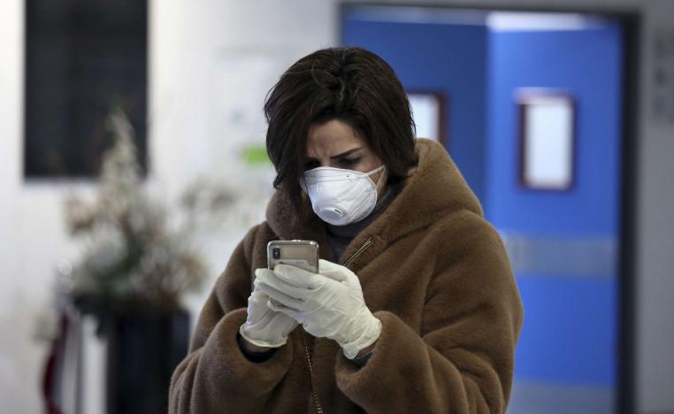 امرأة لبنانية تطالع هاتفها وتضع قناعا واقيا ضد كورونا