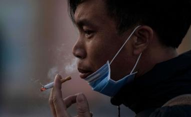 رجل يرفع قناع وجهه لتدخين سيجارة في بكين