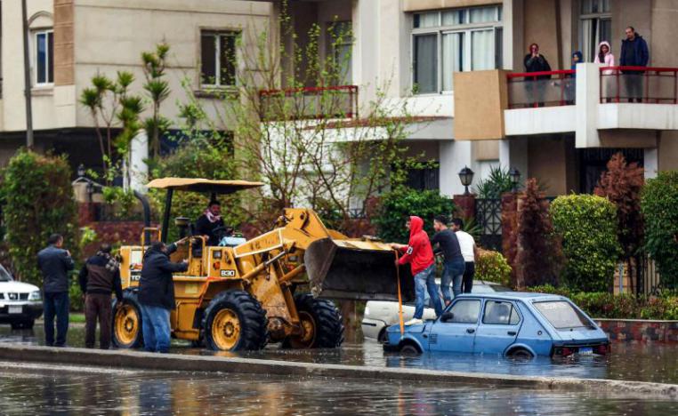 People use a bulldozer to pull out an inundated car from a flooded street in Cairo
