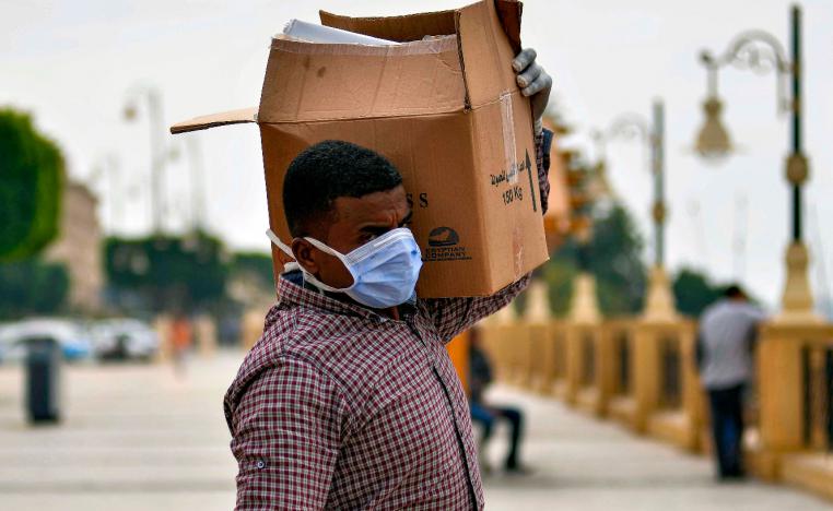A worker on a Nile cruise ship, wearing a protective face mask, walks carrying a box along the corniche overlooking the river bank in Egypt's southern city of Luxor