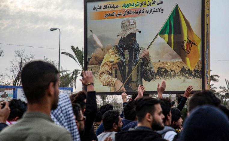 Protesters chant slogans as they walk past a Kata'ib Hezbollah's billboard during an anti-government demonstration in Basra