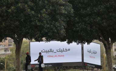 رجلان في بيروت يمران أمام لوحات اعلانية تعرض رسالة تحث المواطنين على البقاء في منازلهم 