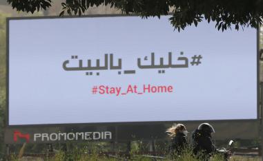 زوجان يمران بجوار لوحة في بيروت تحث المواطنين على البقاء في المنزل 