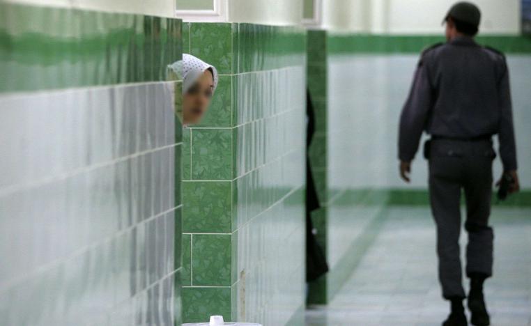 An Iranian inmate peers from behind a wall as a guard walks by