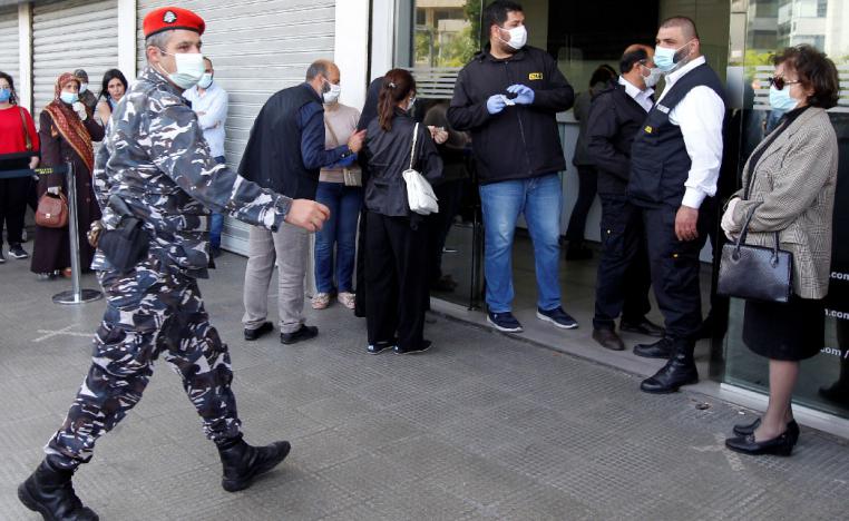 A Lebanese police officer walks near a crowd formed outside a money transfer office