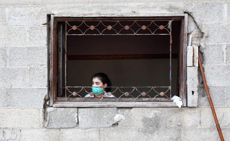 A girl wears a face mask as she looks out of the window in the Gaza Strip