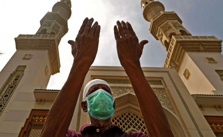 An elderly man wearing a protective mask lifts his hands in prayer outside a closed mosque in Sharjah 