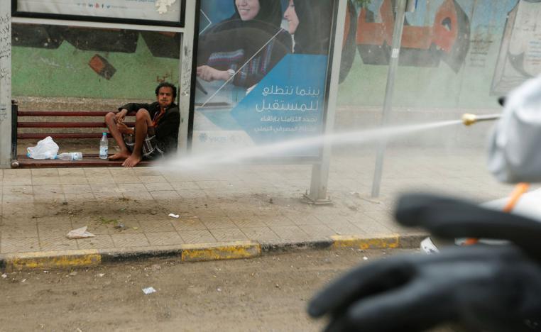 A man sits in an ad frame as health workers disinfect a street in Sanaa, Yemen