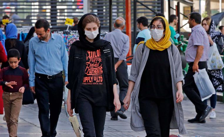 Iranians, some wearing face masks, walk along a street in the capital Tehran