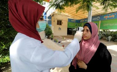 عاملة في مجال الرعاية الصحية تتحقق من درجة حرارة امرأة فلسطينية