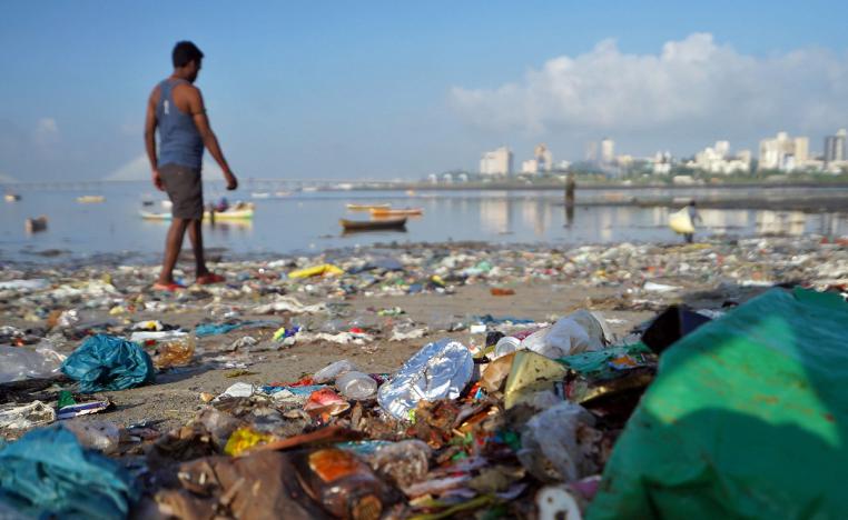 رجل يمشي على شاطئ مليء بالمخلفات البلاستيكية في مومباي بالهند