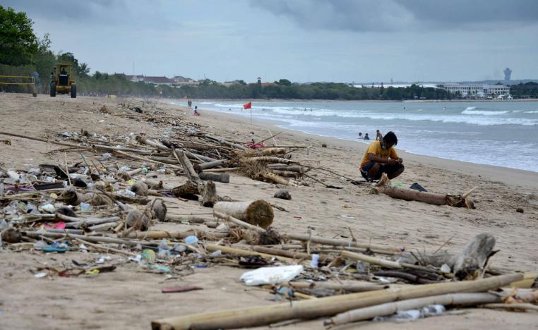 رجل يجلس بالقرب من نفايات بلاستيكية جرفتها الأمواج على شاطئ كوتا في جزيرة بالي الإندونيسية
