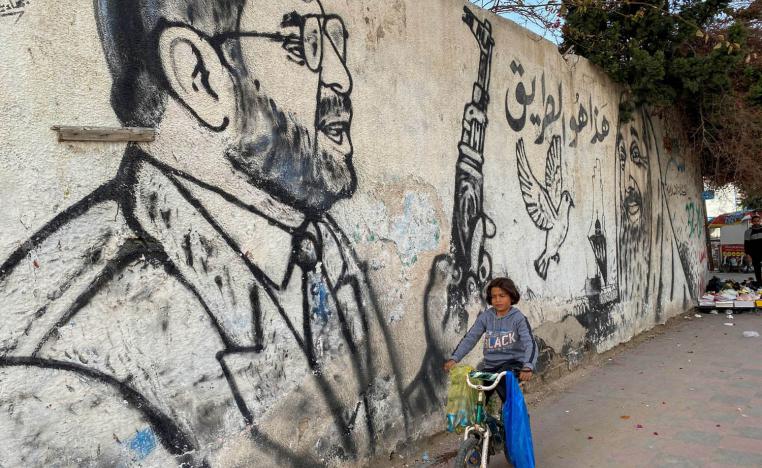 طفل فلسطيني في غزة يمر بالقرب من جدارية لعبد العزيز الرنتيسي يحمل بندقية