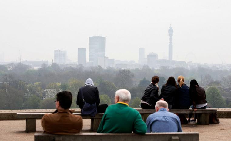 أشخاص يجلسون أعلى تل بريمروز في لندن حيث المدينة أدناه محاطة بالتلوث