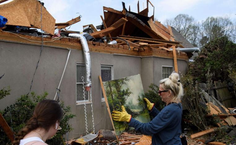 سيدة تلتقط لوحة من حطام منزلها المدمر في مارس 2021 بعد إعصار ضرب ألاباما الأميركية