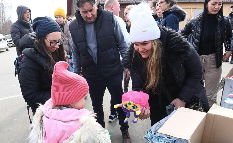 A woman offers a toy to a girl after Ukrainian refugees crossed the Ukrainian-Hungarian border in Tiszabecs