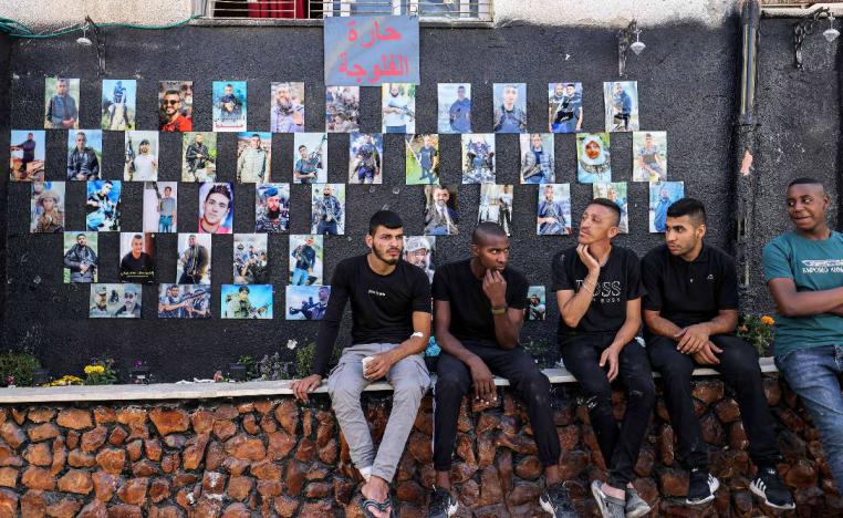 فلسطينيون أمام لوحة تجمع صور شهداء مخيم جنين