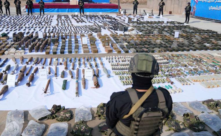 مقاتل من الحشد الشعبي في العراق يستعرض كمية من الأسلحة المصادرة في عملية تفتيش أمنية