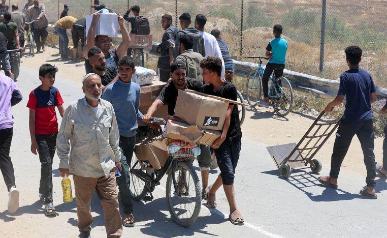 Palestinians walk with aid supplies which they received from the US-backed Gaza Humanitarian Foundation, in the central Gaza Strip