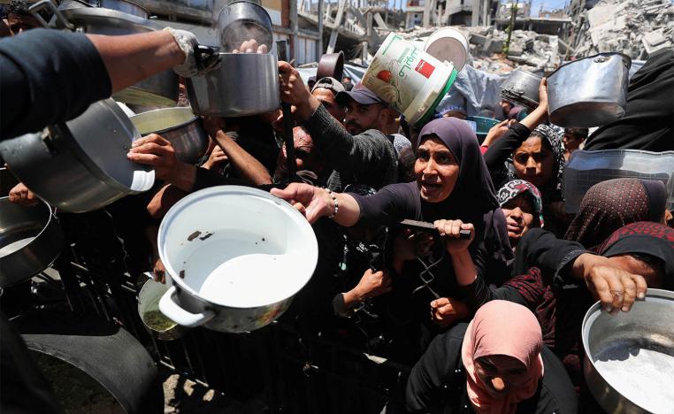 Palestinians wait to receive food cooked by a charity kitchen, in Beit Lahia