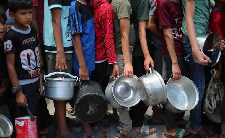 Palestinian boys carry pots as the queue at a hot meal distribution point in Nuseirat in the central Gaza Strip