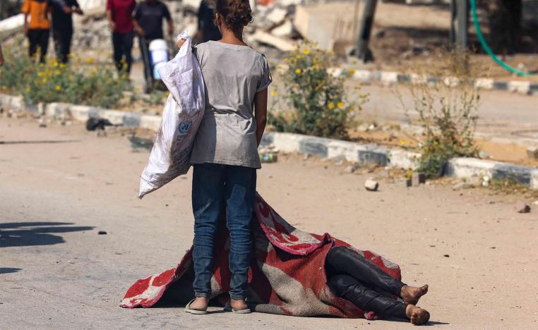 A Palestinian girl stands over the covered body of a person who was killed while seeking food at a distribution point run by the US and Israeli-backed Gaza Humanitarian Foundation group, in Nusseirat