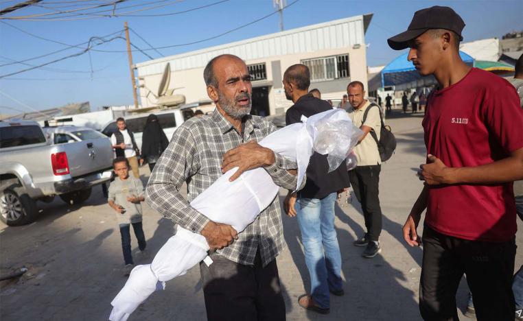 A Palestinian man carries the draped body of a child killed in Israeli strikes the previous day on the central Gaza Strip, outside the Shuhada al-Aqsa hospital