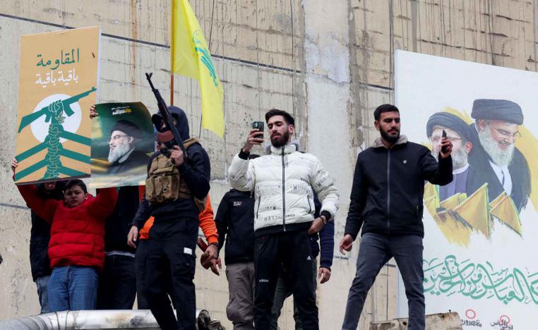 People stand near a poster depicting late Hezbollah leader Sayyed Hassan Nasrallah and late senior Hezbollah official Hashem Safieddine as one of them carries a weapon, in Beirut’s southern suburbs, November 27, 2024. 
