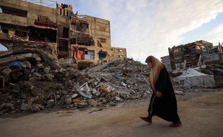 A Palestinian woman walks past residential buildings damaged and destroyed during the war, in Gaza City, December 14, 2025. 