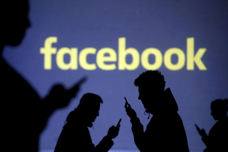 شعار فيسبوك في خلفية مستخدمين يمسكون هواتفهم الذكية