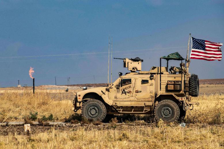 A US armoured vehicle drives past a burning gas flare from oil extraction